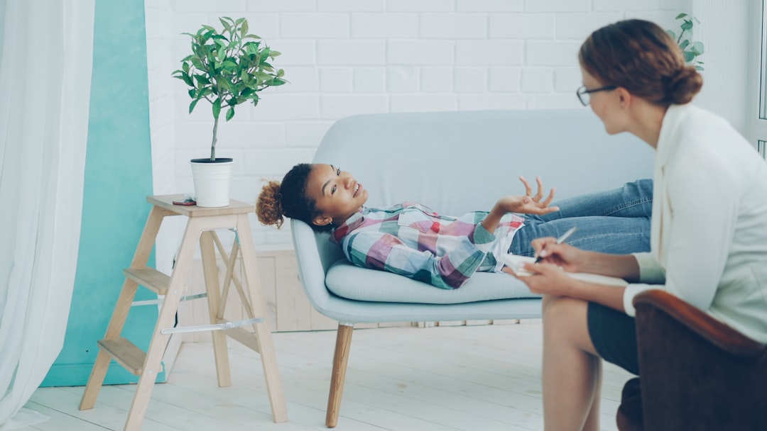 Relaxed African American teenager is talking to psychologist lying on couch and smiling while therapist is listening and taking notes. Young people, mental health and profession concept.