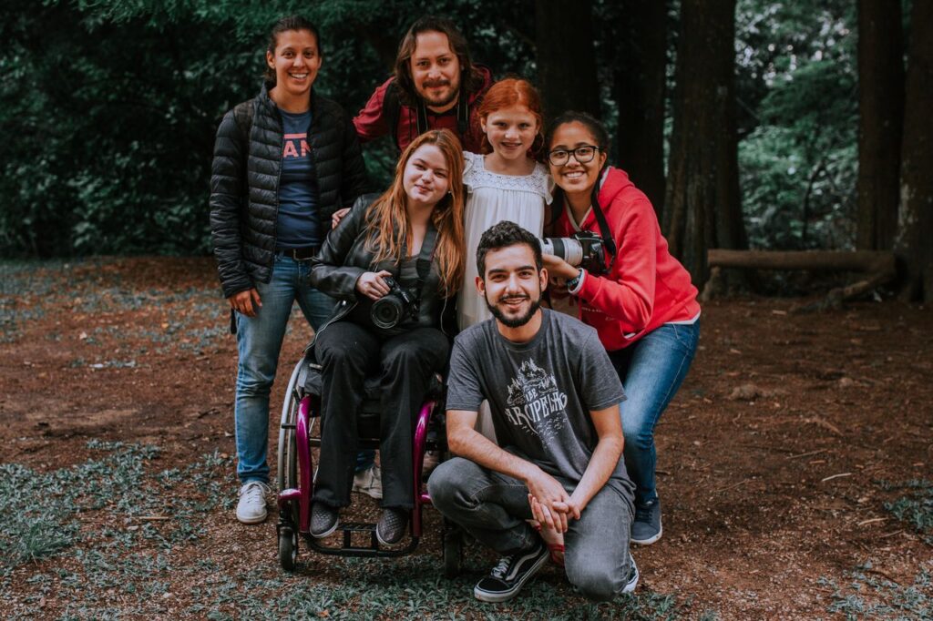 Group of friends smiling and posing with a camera in a forest setting, embracing diversity.