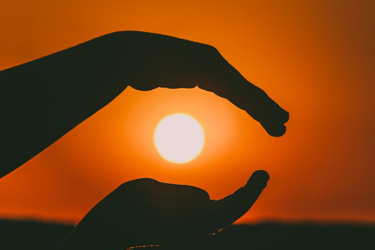 Silhouetted hands in a sunset scene capturing the suns glow.